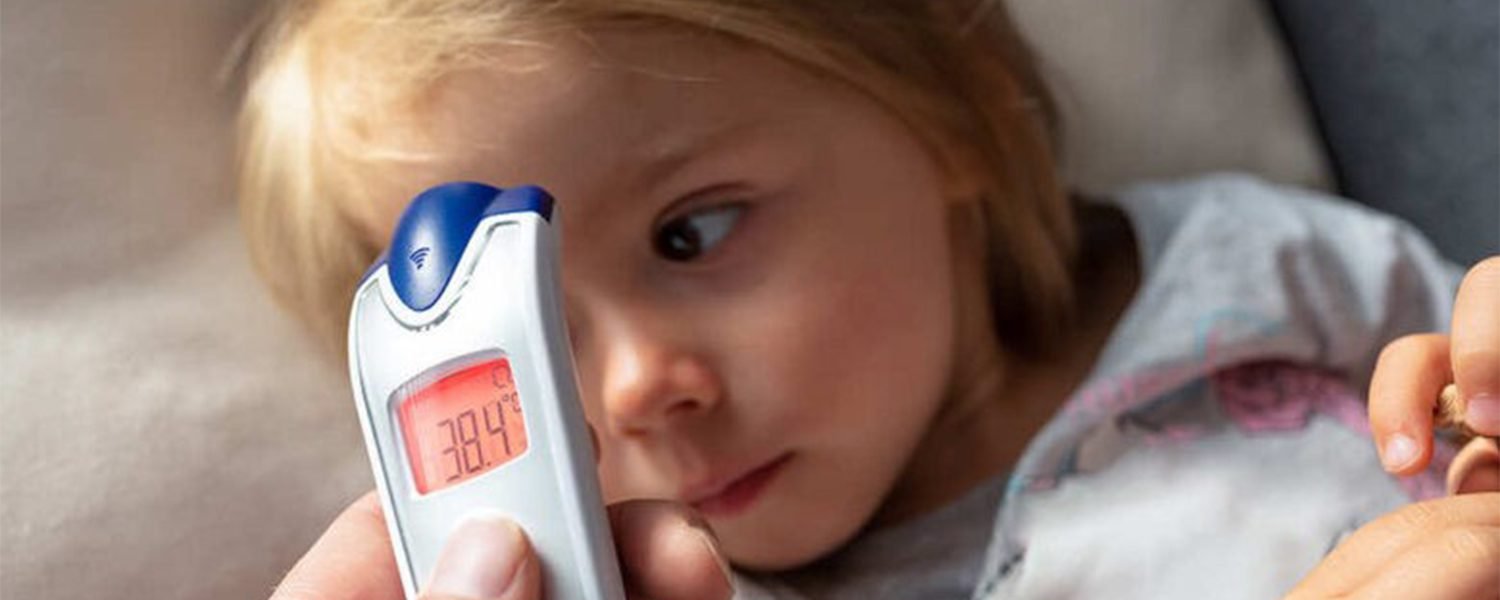 A toddler lying down while an adult takes their temperature with a digital thermometer
